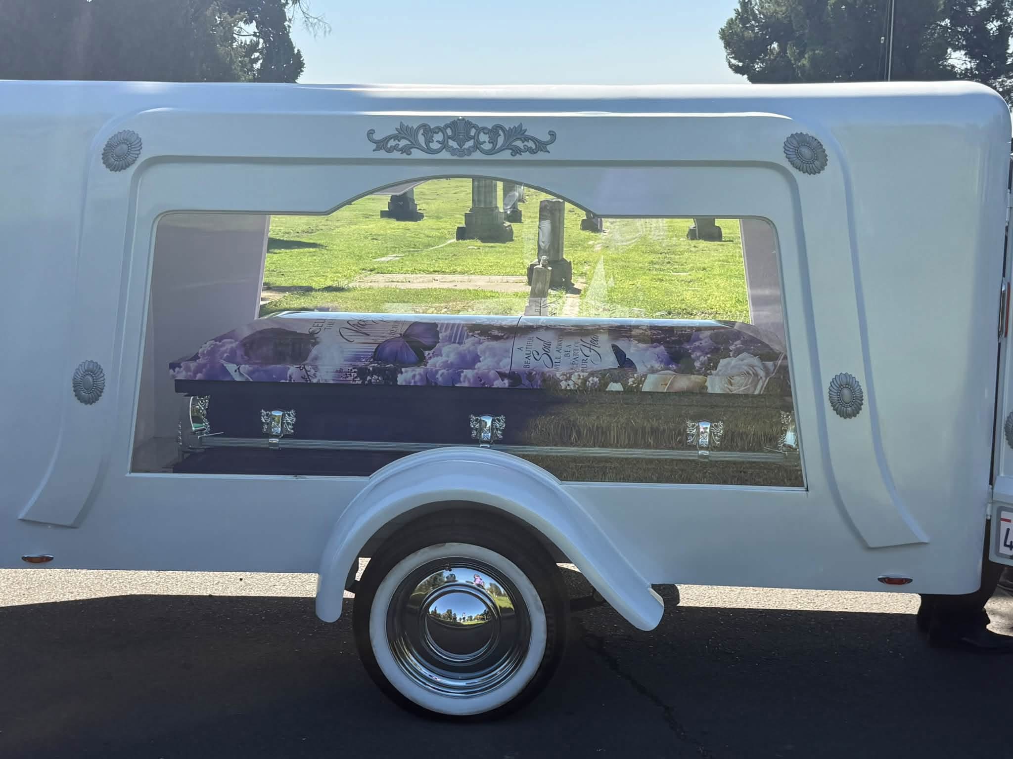 White hearse trailer displaying a purple memorial casket